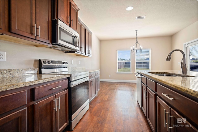 kitchen with hanging light fixtures, sink, dark wood-type flooring, appliances with stainless steel finishes, and light stone countertops