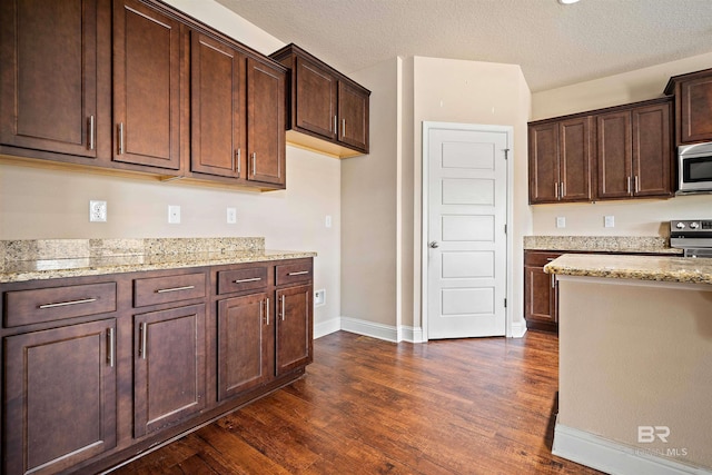 kitchen featuring dark wood-type flooring, light stone countertops, appliances with stainless steel finishes, and a textured ceiling