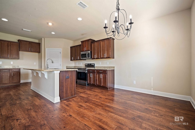 kitchen with light stone counters, an island with sink, dark wood-type flooring, appliances with stainless steel finishes, and a breakfast bar area