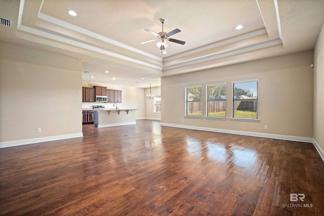 unfurnished living room with ceiling fan, a raised ceiling, crown molding, and dark wood-type flooring