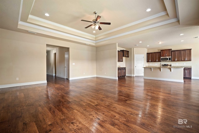 unfurnished living room with ceiling fan, a tray ceiling, crown molding, and dark hardwood / wood-style flooring