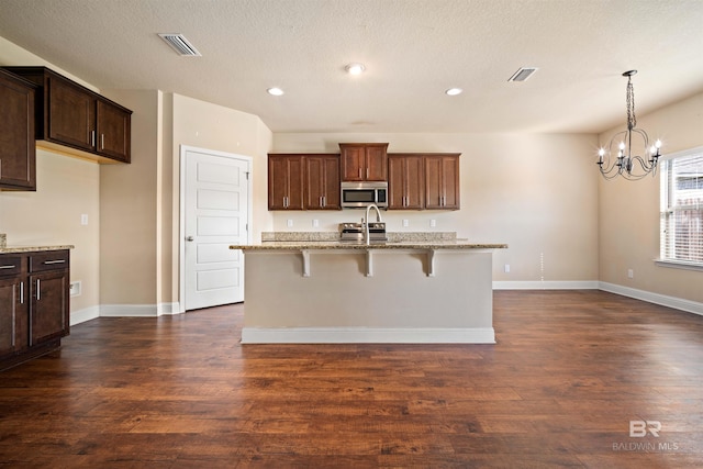 kitchen with an island with sink, a textured ceiling, light stone countertops, a kitchen bar, and dark hardwood / wood-style flooring