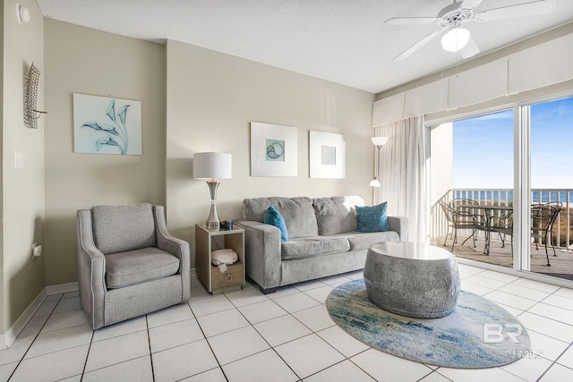 living room featuring ceiling fan, a water view, light tile patterned floors, and a textured ceiling