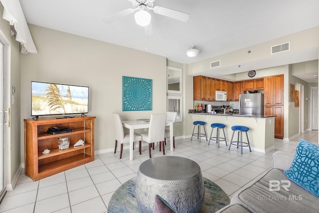 kitchen featuring ceiling fan, kitchen peninsula, a kitchen bar, light tile patterned flooring, and appliances with stainless steel finishes