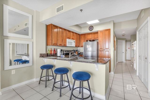 kitchen featuring kitchen peninsula, dark stone countertops, a kitchen bar, light tile patterned flooring, and appliances with stainless steel finishes