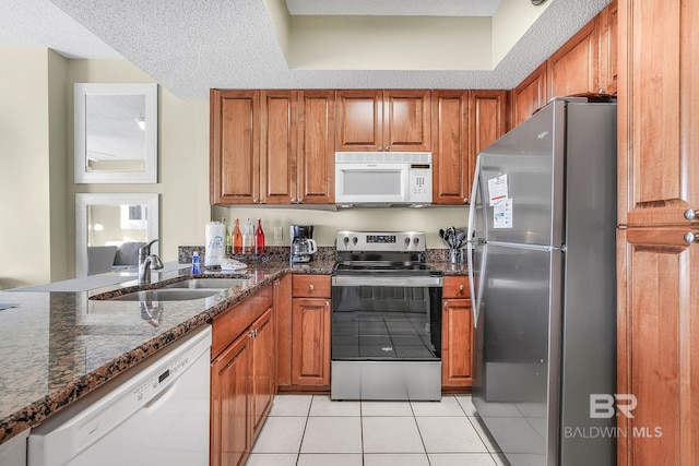 kitchen with sink, dark stone countertops, a textured ceiling, light tile patterned flooring, and stainless steel appliances