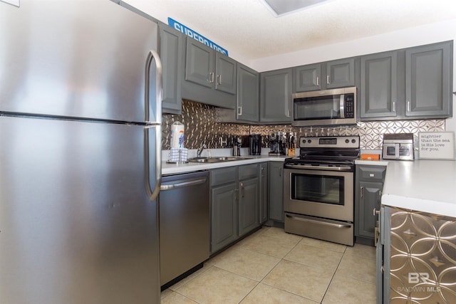 kitchen featuring decorative backsplash, gray cabinets, light tile patterned floors, and appliances with stainless steel finishes