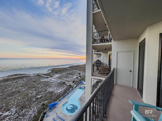 balcony at dusk featuring a beach view and a water view