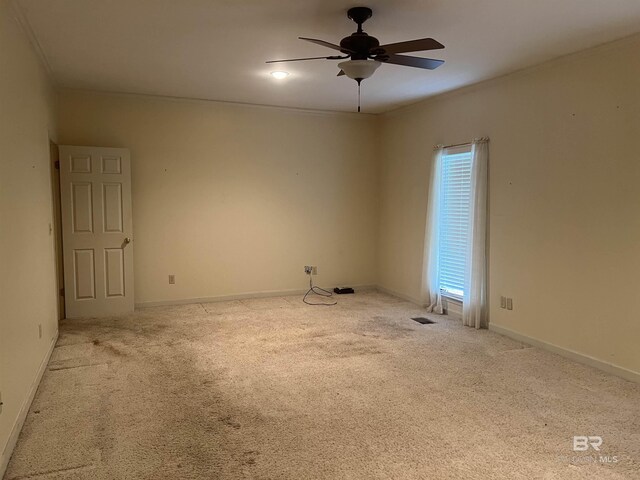 carpeted empty room with a ceiling fan, crown molding, and baseboards