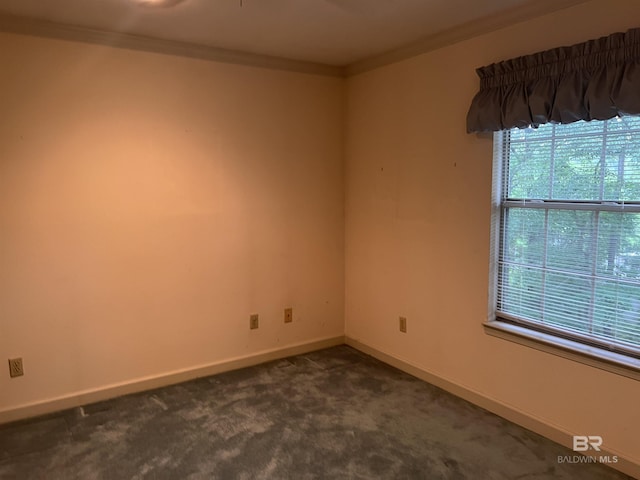 empty room featuring dark carpet, baseboards, and crown molding