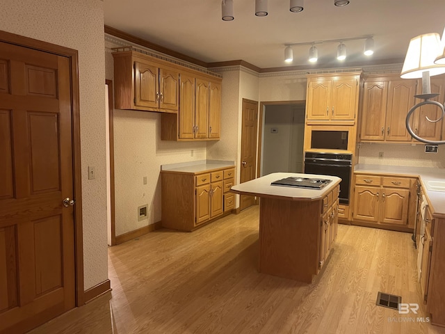 kitchen with black oven, a kitchen island, light wood-style floors, light countertops, and crown molding