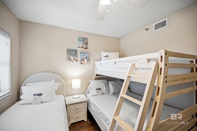 bedroom with dark wood-style floors, a textured ceiling, visible vents, and a ceiling fan