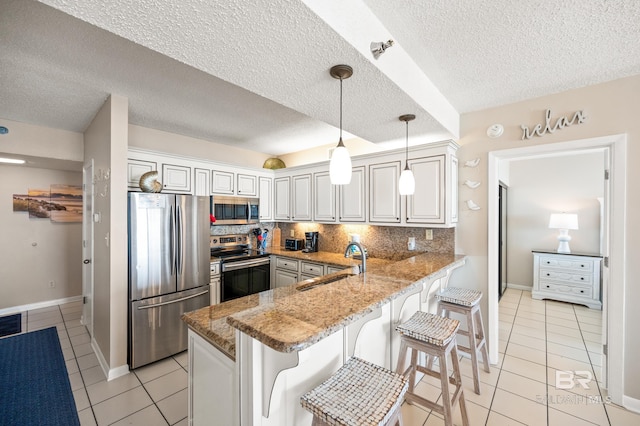 kitchen with light stone counters, a peninsula, a sink, appliances with stainless steel finishes, and tasteful backsplash