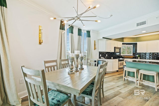 dining room with light wood-type flooring, crown molding, and a notable chandelier