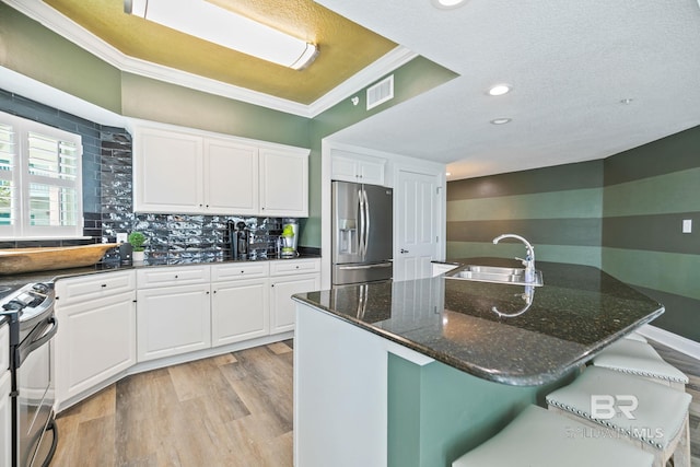 kitchen with stainless steel appliances, a breakfast bar, sink, dark stone counters, and white cabinets