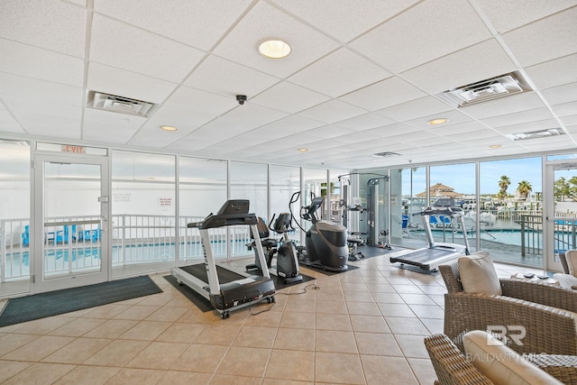 exercise room featuring a water view, light tile patterned flooring, floor to ceiling windows, and a drop ceiling