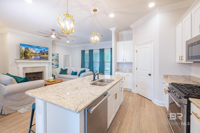 kitchen with a fireplace, light wood-type flooring, sink, a kitchen island with sink, and appliances with stainless steel finishes