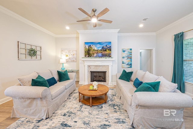 living room featuring a premium fireplace, wood-type flooring, ornamental molding, and ceiling fan