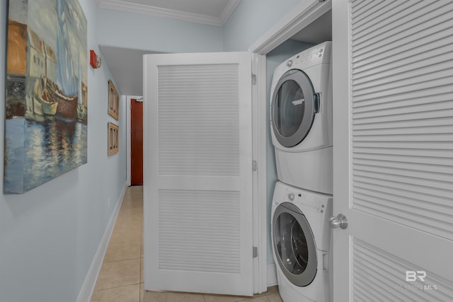 laundry room featuring light tile patterned floors, baseboards, laundry area, stacked washer and clothes dryer, and crown molding