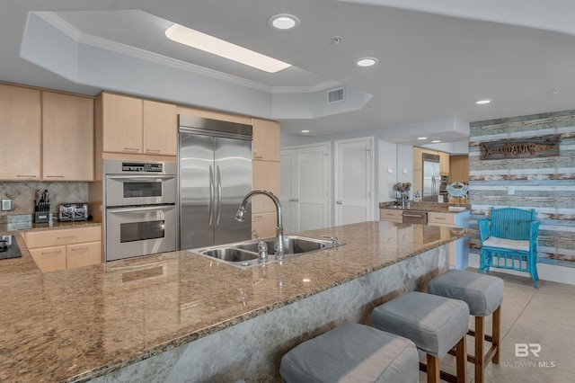 kitchen featuring light brown cabinets, stainless steel appliances, a tray ceiling, and a sink