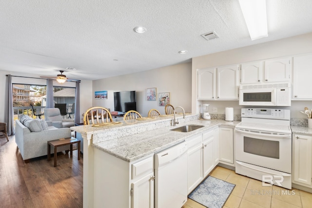 kitchen featuring white appliances, visible vents, a peninsula, a sink, and open floor plan