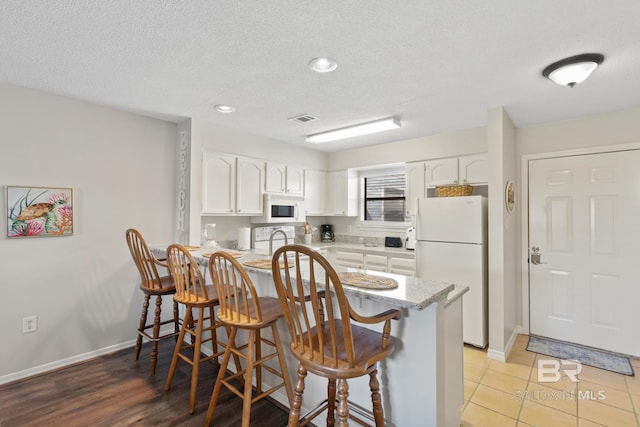 kitchen featuring a kitchen bar, white appliances, a peninsula, and white cabinetry