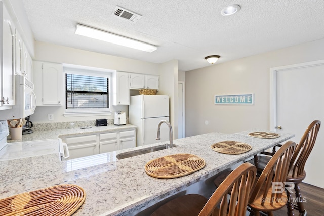 kitchen featuring white appliances, light stone counters, visible vents, a breakfast bar, and a sink