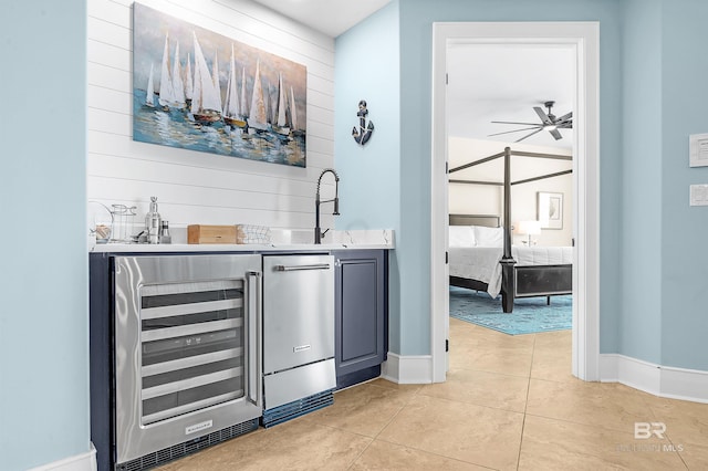 bar featuring light tile patterned floors, beverage cooler, a sink, a ceiling fan, and baseboards