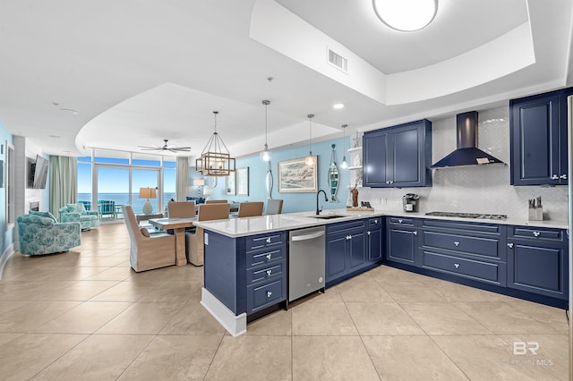 kitchen featuring wall chimney exhaust hood, appliances with stainless steel finishes, decorative light fixtures, and blue cabinets