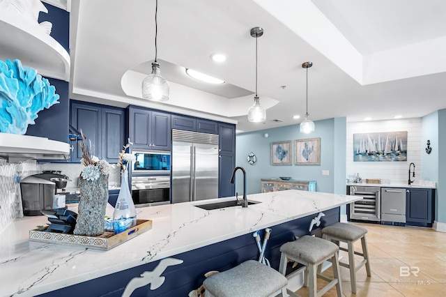 kitchen featuring a raised ceiling, built in appliances, blue cabinets, a kitchen bar, and a sink