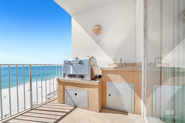 balcony with a beach view, area for grilling, a water view, exterior kitchen, and a sink