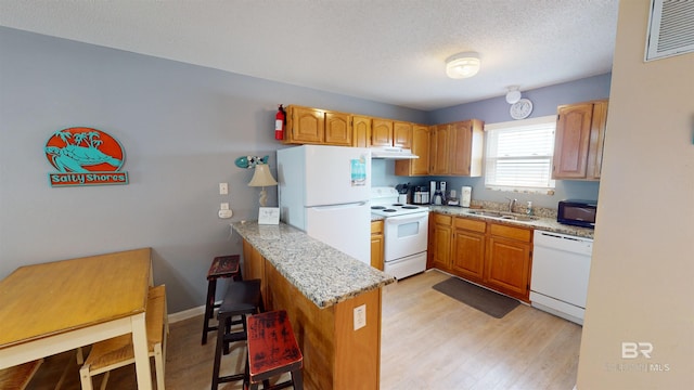 kitchen with light wood-type flooring, sink, kitchen peninsula, a kitchen bar, and white appliances