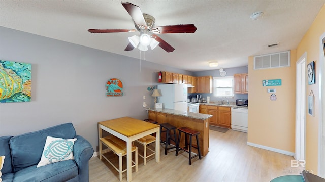 kitchen featuring a kitchen breakfast bar, light hardwood / wood-style floors, white appliances, kitchen peninsula, and ceiling fan