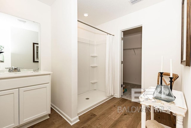 full bathroom featuring wood finished floors, vanity, baseboards, a spacious closet, and a shower stall