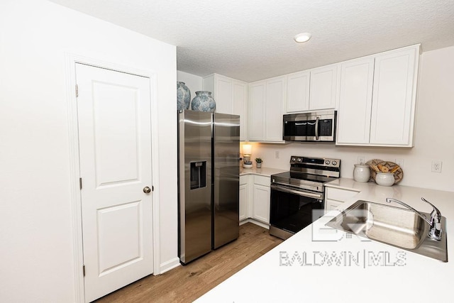 kitchen with stainless steel appliances, light countertops, light wood-style floors, white cabinets, and a sink