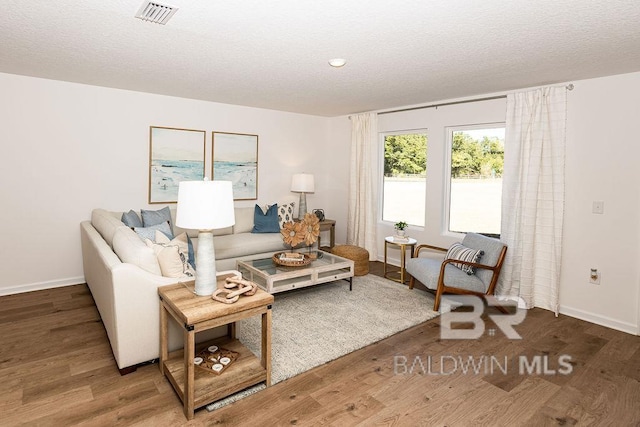 living room featuring a textured ceiling, wood finished floors, visible vents, and baseboards