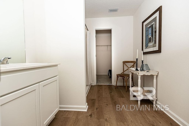 hall with visible vents, baseboards, dark wood-style flooring, a textured ceiling, and a sink