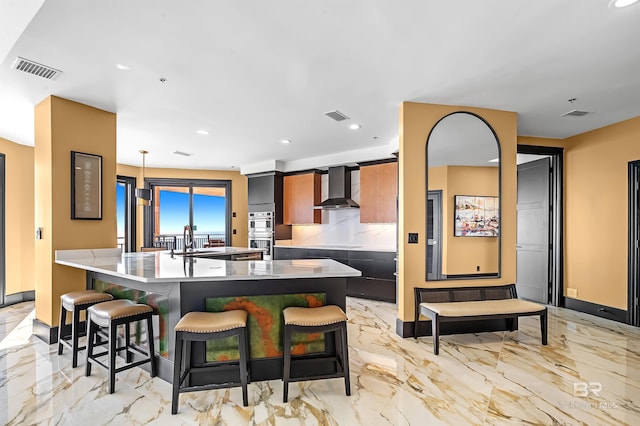 kitchen with marble finish floor, visible vents, a sink, wall chimney range hood, and a kitchen bar