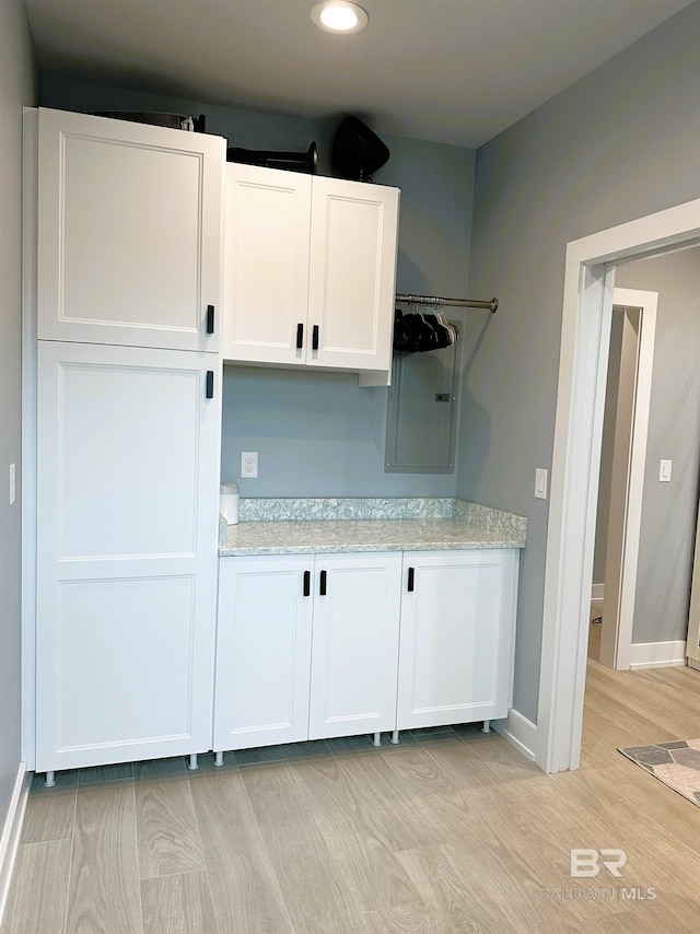 kitchen with light stone countertops, electric panel, light hardwood / wood-style flooring, and white cabinetry