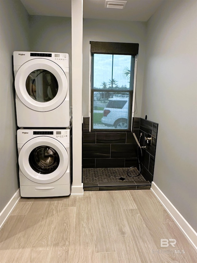 clothes washing area featuring light hardwood / wood-style floors and stacked washer / drying machine