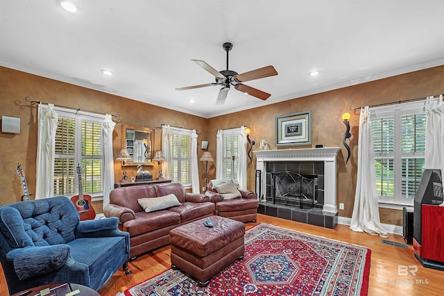 living room with ceiling fan, a tiled fireplace, a wealth of natural light, and wood-type flooring