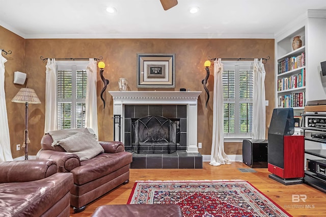 living room with a fireplace, built in features, ornamental molding, and hardwood / wood-style floors