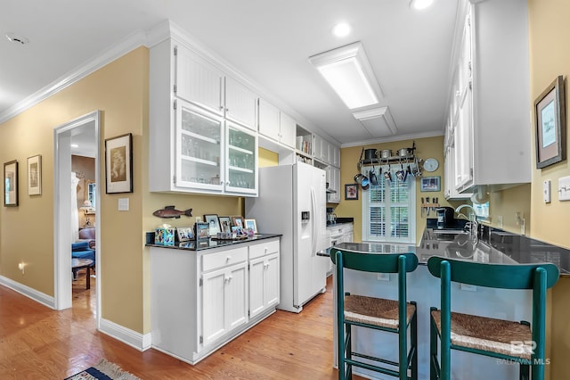 kitchen with light hardwood / wood-style floors, a kitchen bar, ornamental molding, and white cabinetry