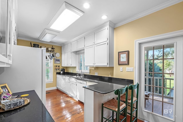 kitchen with white cabinets, kitchen peninsula, light hardwood / wood-style flooring, dishwasher, and crown molding