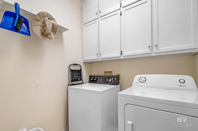 clothes washing area with separate washer and dryer and cabinets