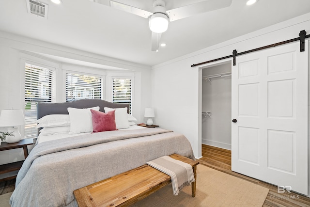 bedroom with a walk in closet, ceiling fan, a barn door, hardwood / wood-style floors, and a closet