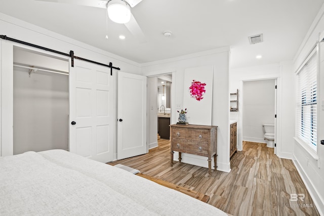 bedroom with ensuite bath, ceiling fan, a barn door, a closet, and light wood-type flooring