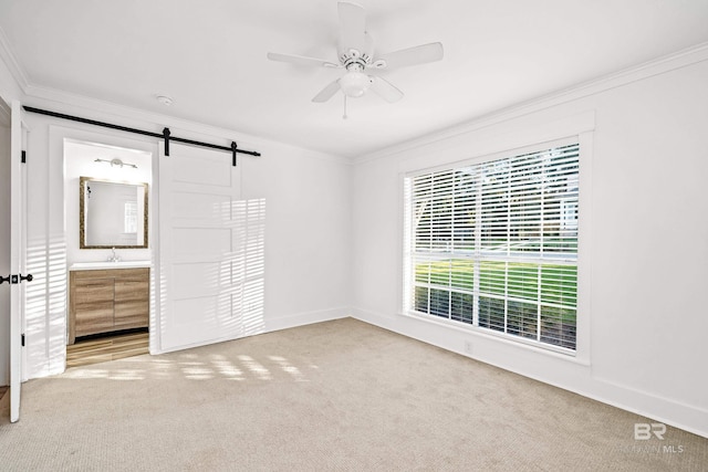 unfurnished bedroom with light carpet, crown molding, ceiling fan, a barn door, and connected bathroom