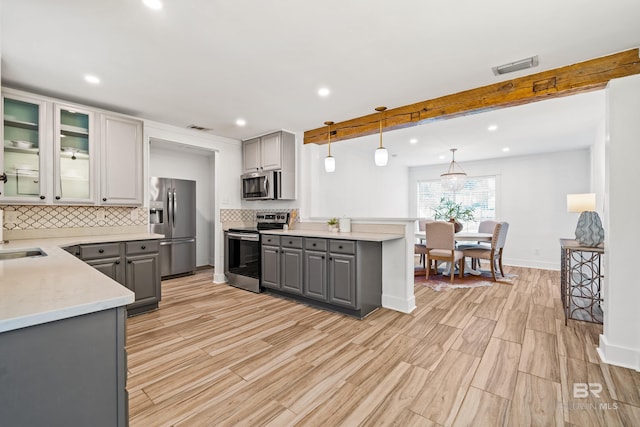 kitchen with appliances with stainless steel finishes, gray cabinets, hanging light fixtures, and beam ceiling