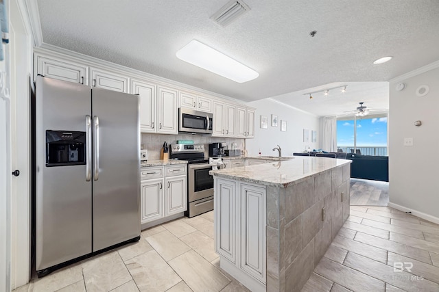 kitchen featuring light stone countertops, white cabinetry, stainless steel appliances, ornamental molding, and a center island with sink